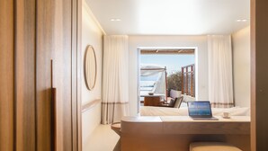 A modern hotel room with a wooden floor, a bed with a laptop, a small table, and a view of the sea. - Avgoustos Suites - Adults only (Naxos)