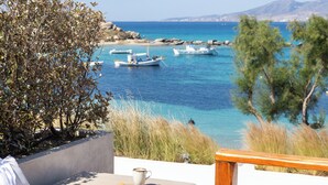 A terrace with a table, a hat, and a plate of croissants, overlooking a coastal area with boats and greenery. - Avgoustos Suites - Adults only (Naxos)
