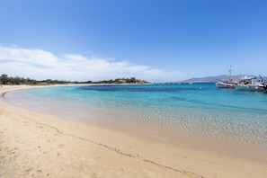 A beach with clear turquoise water, a sandy shore, and boats docked near the water. - Avgoustos Suites - Adults only (Naxos)