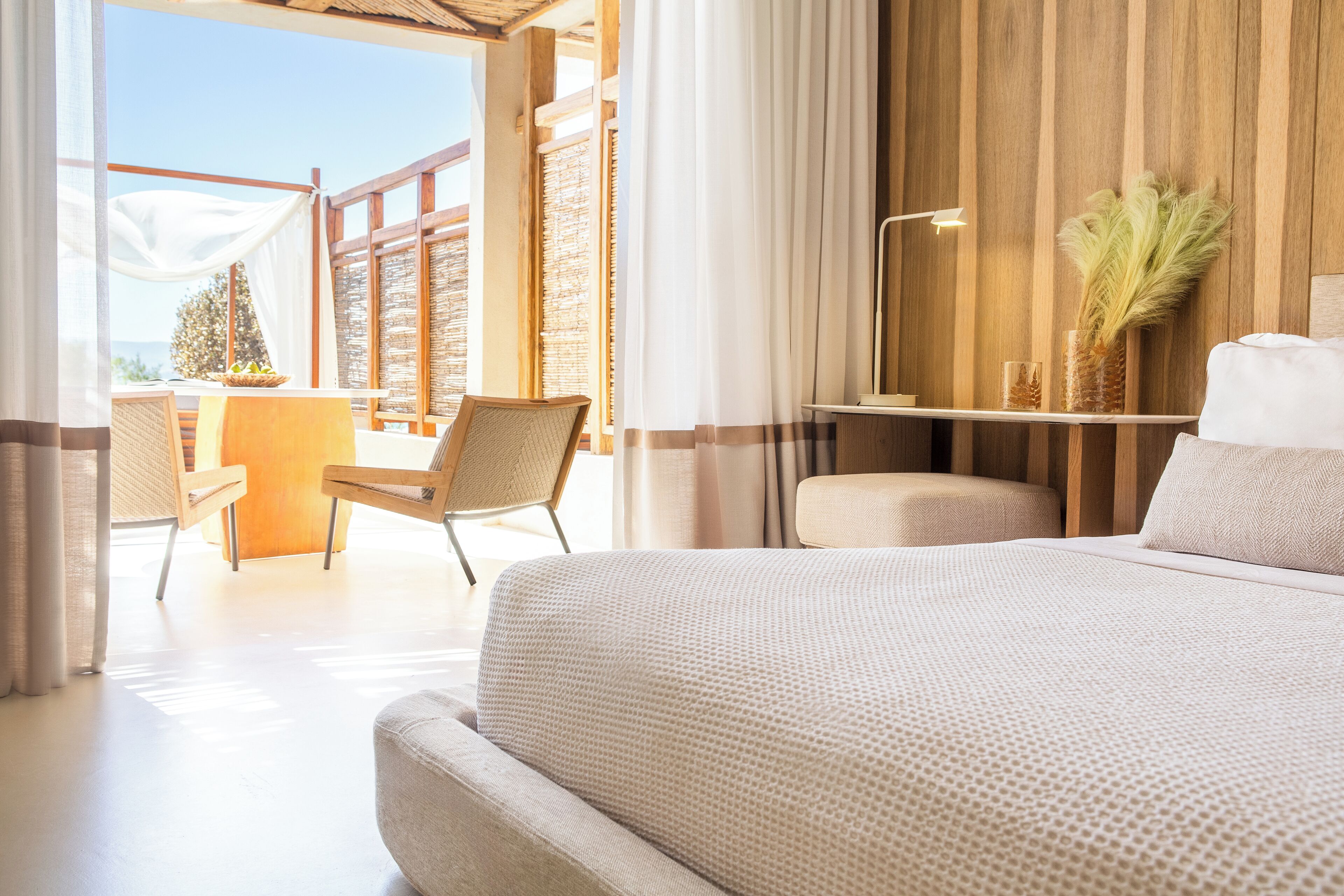 Habitación de hotel con una cama grande, un escritorio y una silla. Se ve el exterior a través de las ventanas.