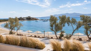 A beachside resort with sun loungers, umbrellas, and a view of the sea and distant mountains. - Avgoustos Suites - Adults only (Naxos)