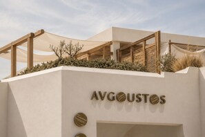 A building with the name 'AVGOUSTOS' on the facade, wooden beams, and a covered outdoor area with plants. - Avgoustos Suites - Adults only (Naxos)