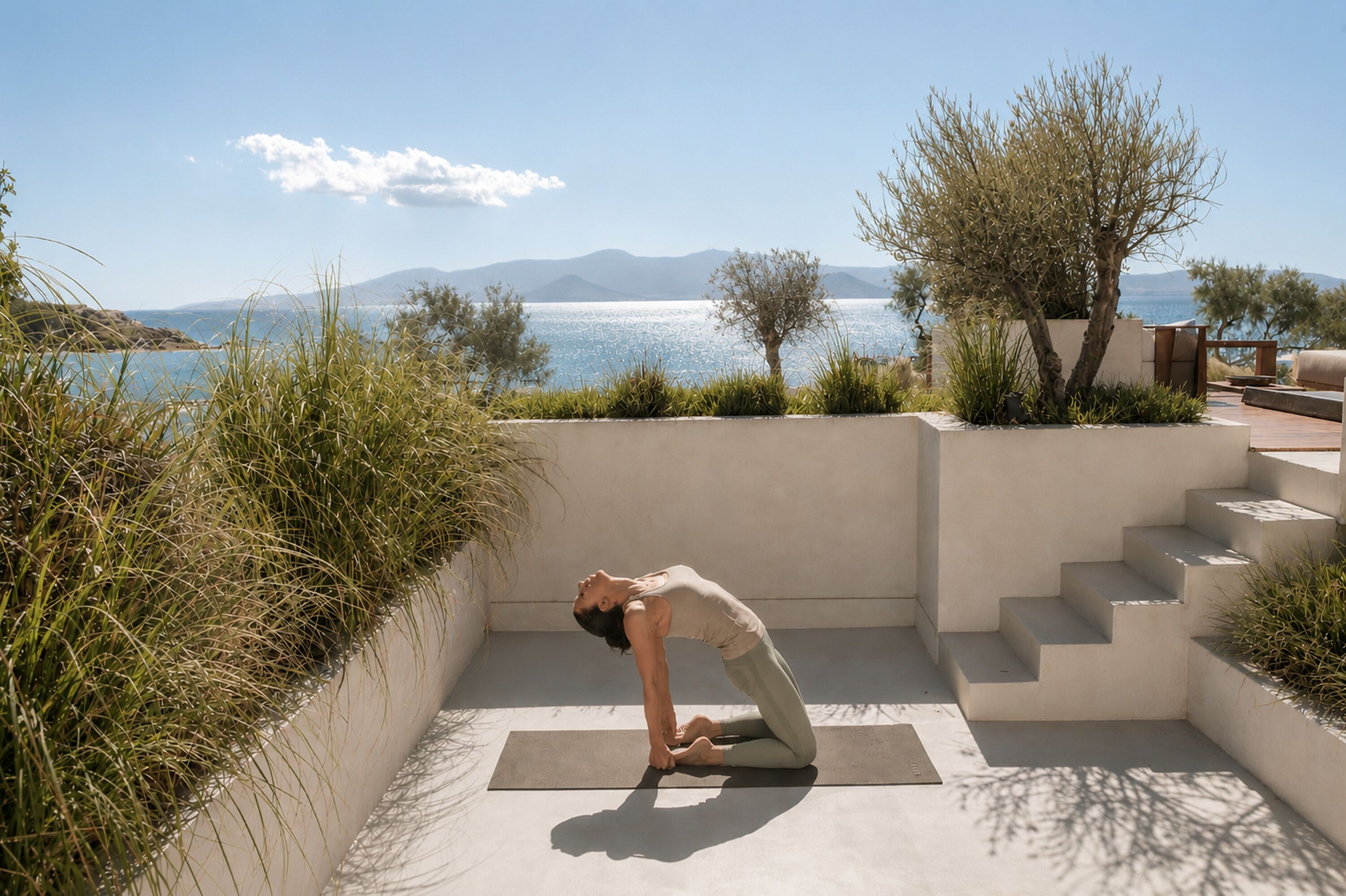 A person performing a yoga pose on a mat in a sunlit outdoor area with a view of the sea and mountains in the background.
