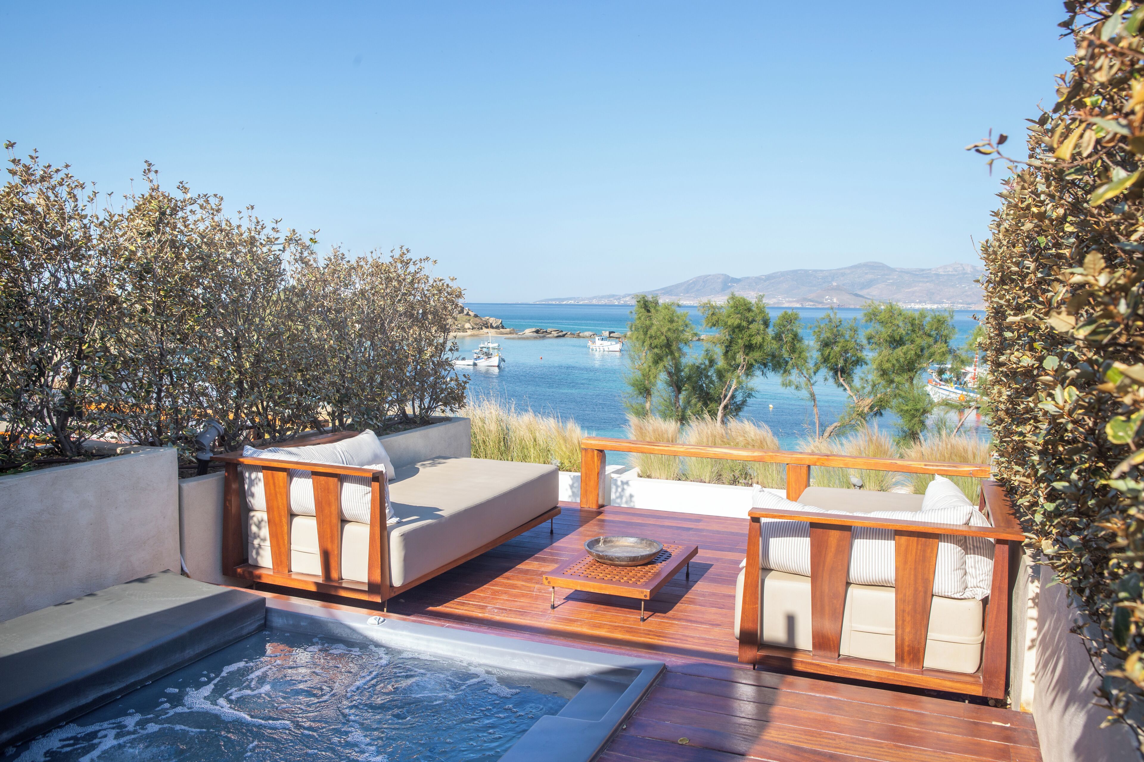 Um terraço com área de estar externa, banheira de hidromassagem e vista para o mar e barcos.