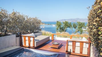 Um terraço com área de estar externa, banheira de hidromassagem e vista para o mar e barcos.