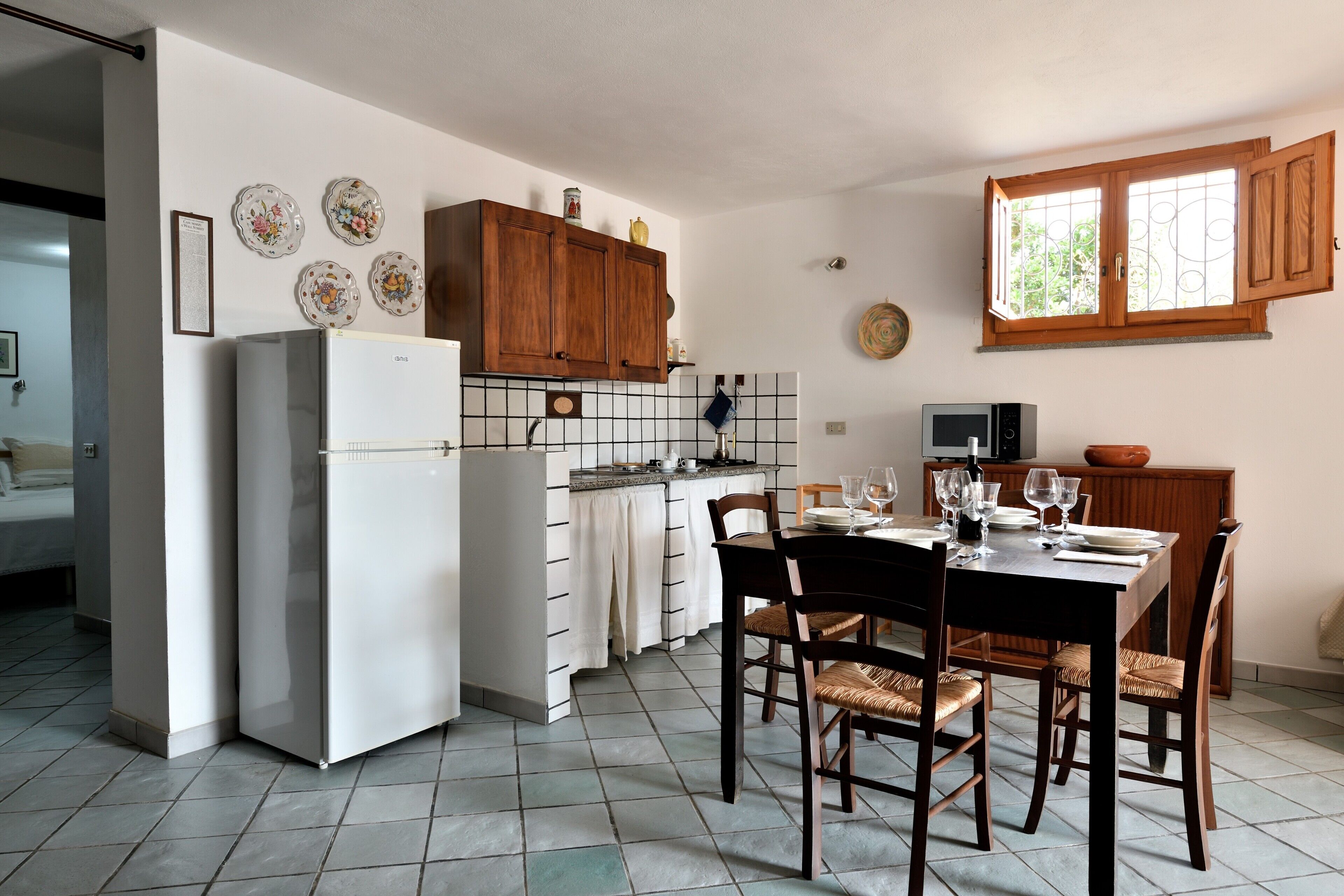 A kitchen with a refrigerator, stove, wooden cabinets, a dining table with chairs, and a window with bars.