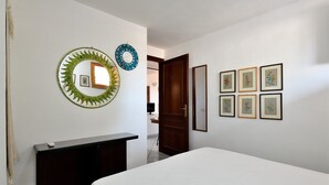 Ein Schlafzimmer mit einem Bett, einem Schminktisch, einem Spiegel und gerahmten Kunstwerken an der Wand.