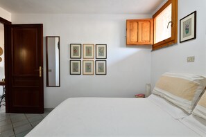 Une chambre à coucher avec un lit, une porte en bois, un miroir et des œuvres d’art florales encadrées accrochées au mur.