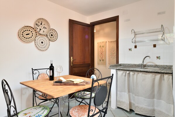 Un comedor con una mesa de madera, sillas de metal, una botella de vino y una tabla de cortar.