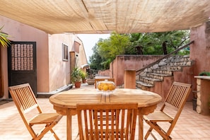 A wooden table with chairs, a fruit display, and a staircase in a covered outdoor area.