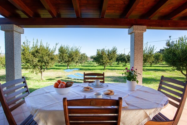 An outdoor patio with a table set for two, surrounded by wooden chairs, under a wooden pergola.