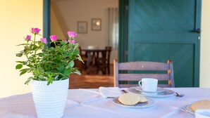 A dining table with a white tablecloth, a white pot with pink flowers, and a green door in the background. - Holiday Home Casa Barvis with Garden, A/C, Terrace and Wi-Fi (Orosei)
