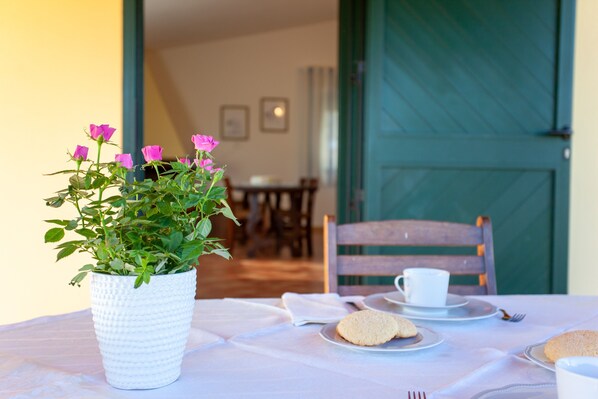 A dining table with a white tablecloth, a white pot with pink flowers, and a green door in the background.