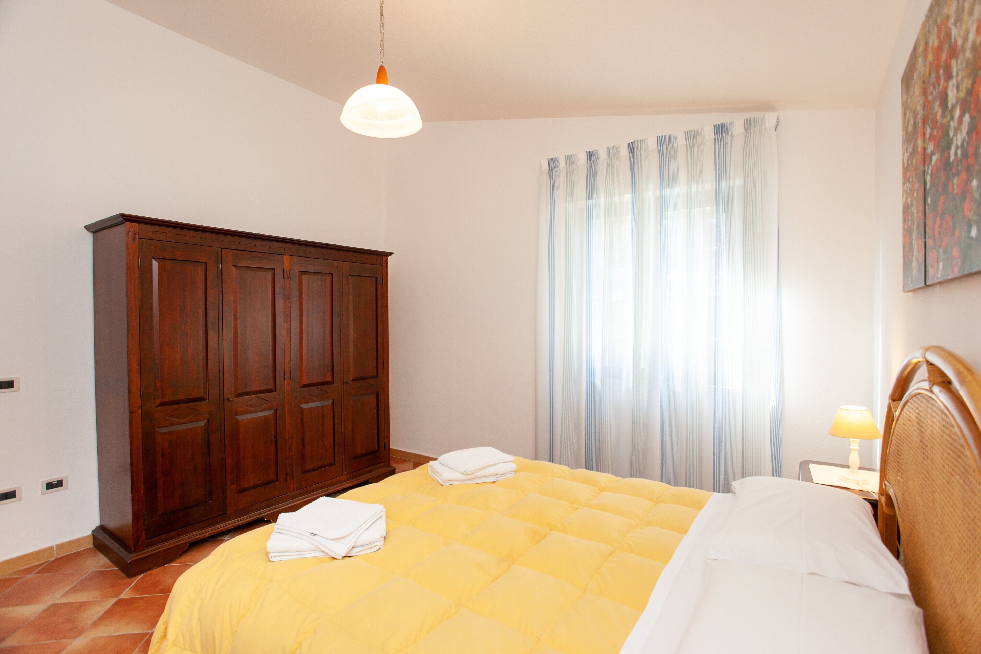 A bedroom with a bed, a wardrobe, a window with curtains, and a painting on the wall.