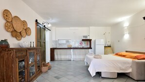 Quarto com cama, armário de madeira, área de cozinha e chão revestido de azulejos.