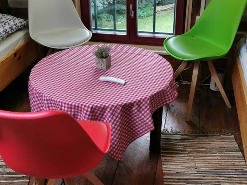 A round table with a checkered tablecloth, two chairs, a small potted plant, and a window with a view of greenery.
