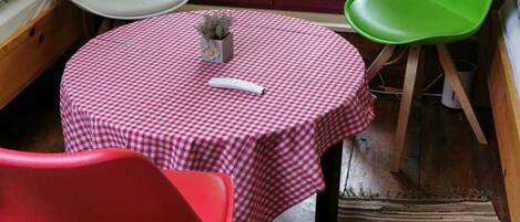 Een ronde tafel met een geruit tafelkleed, twee stoelen, een kleine potplant en een raam met uitzicht op groen.