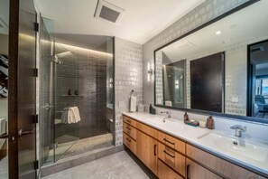 A modern bathroom with a glass-enclosed shower, a large mirror, and wooden cabinetry. - One Snowmass East 303 (Snowmass)