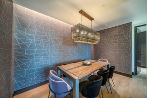 A dining area with a geometric-patterned wall, a wooden table, and modern chairs. - One Snowmass East 303 (Snowmass)