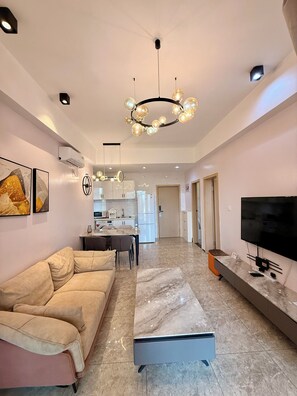 A modern living room with a sofa, a coffee table, a TV, and a kitchen in the background. - Rose Garden Private Apartment By LINK (Kigali)