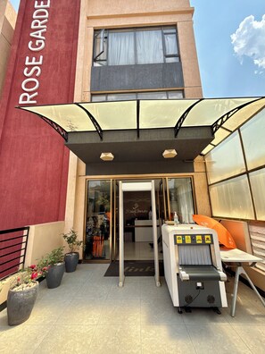 A hotel entrance with a red facade, a covered outdoor seating area, and a reception desk. - Rose Garden Private Apartment By LINK (Kigali)