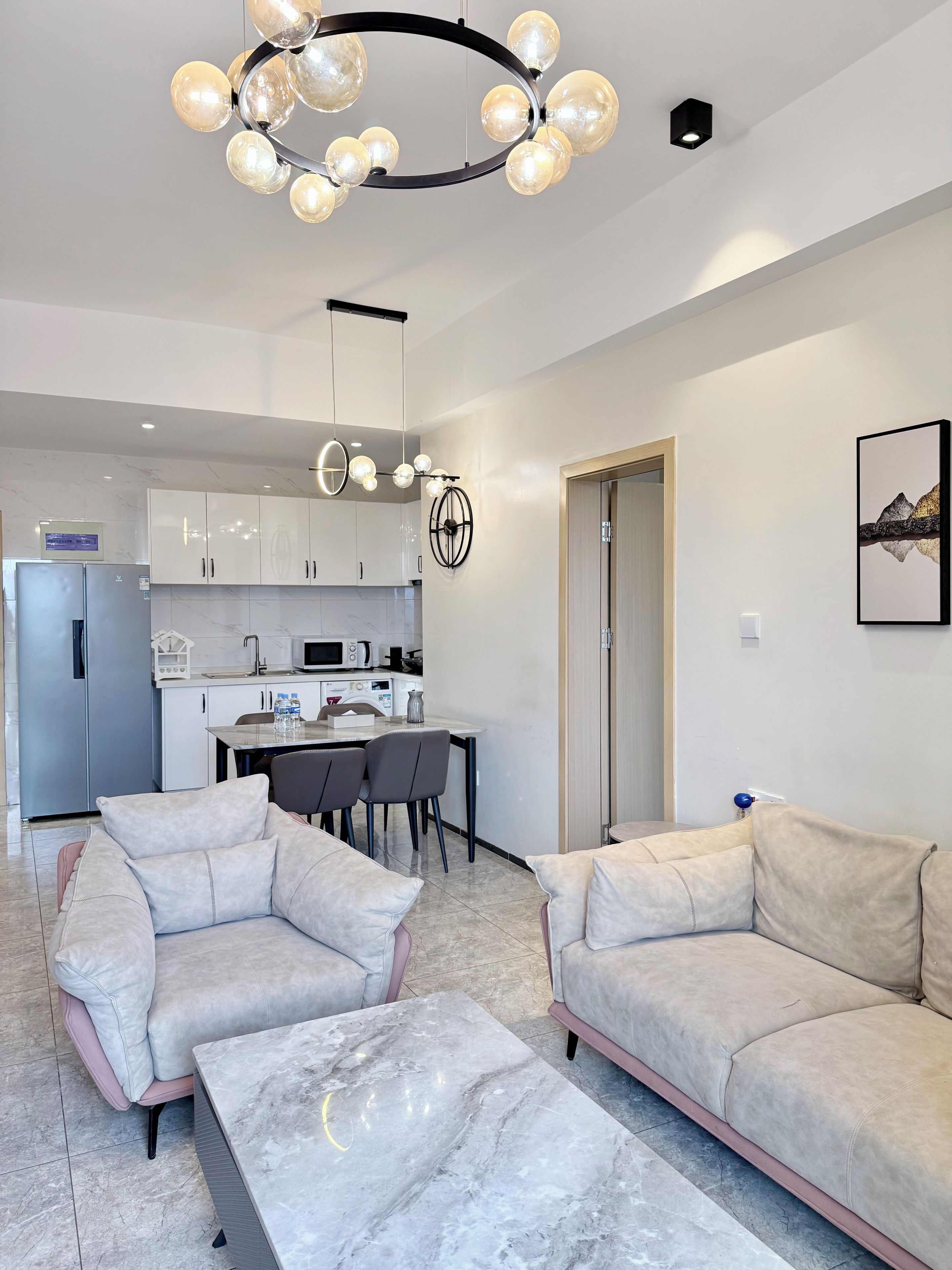 A modern living room with a sofa, a coffee table, and a dining area with chairs and a kitchen in the background.