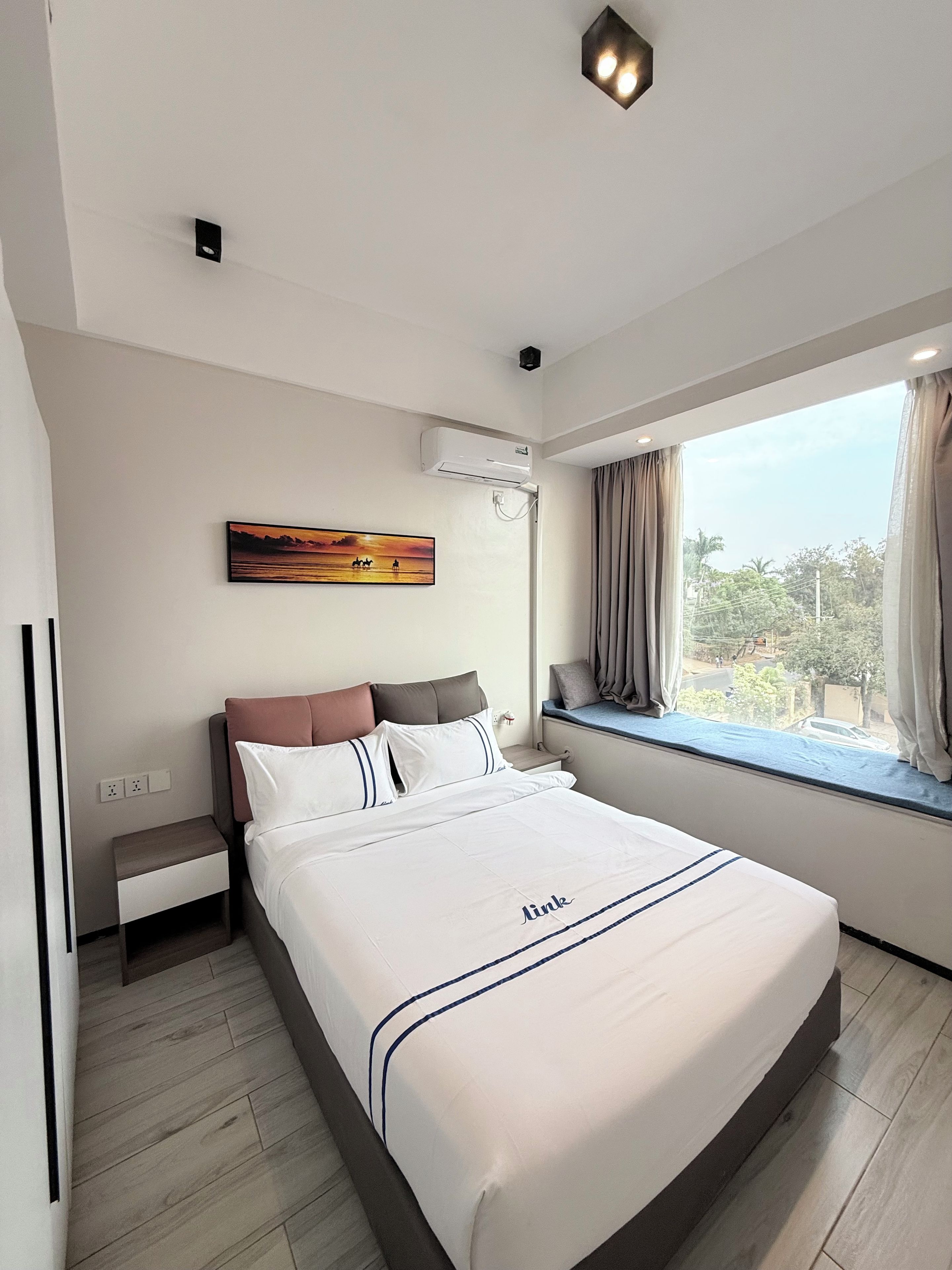 Une chambre d’hôtel avec un lit, une fenêtre avec des rideaux, un tableau au mur et un appareil de climatisation.