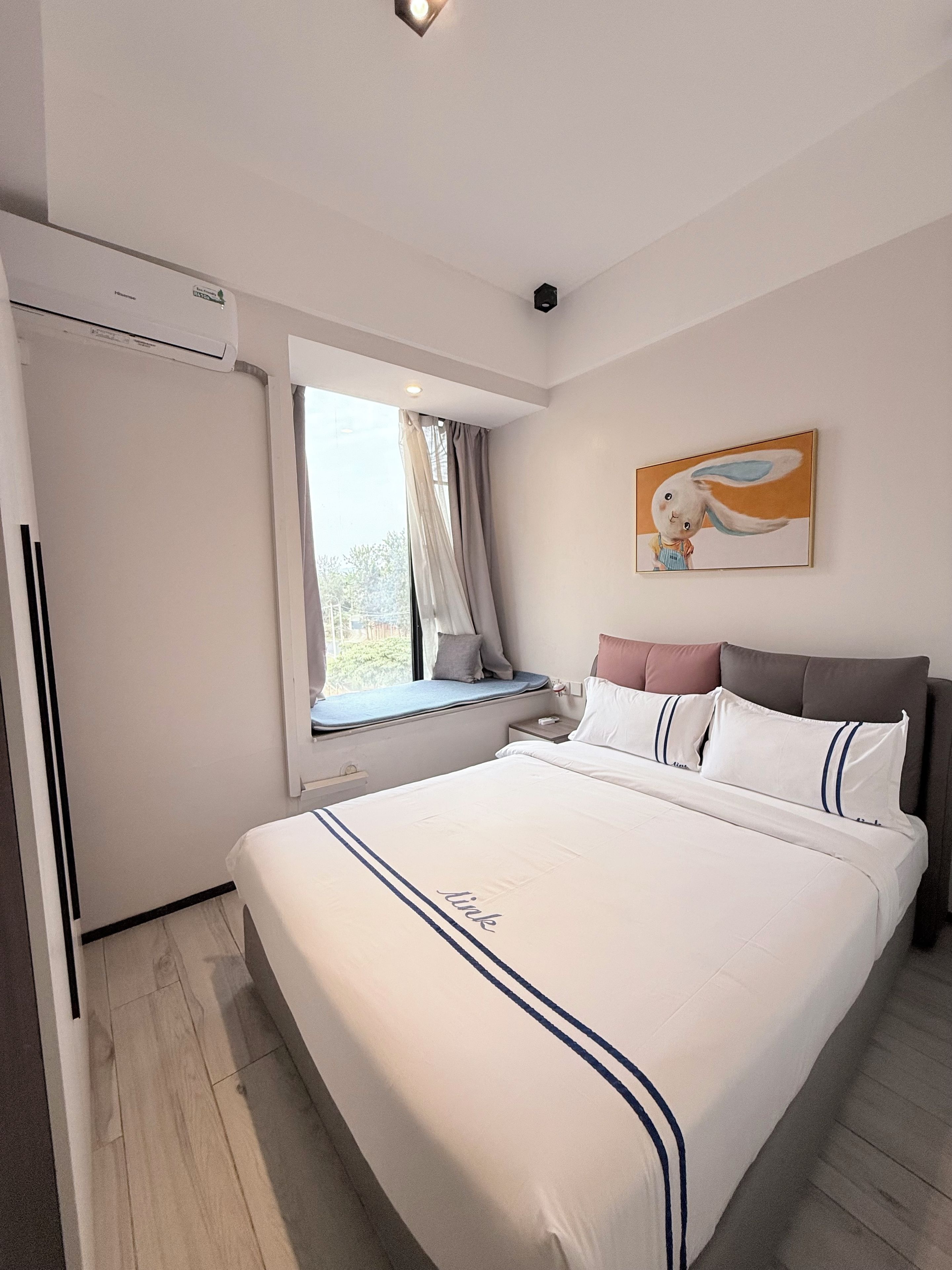 Un dormitorio con una cama grande, una ventana con cortinas, un cuadro en la pared y una lámpara en el techo.