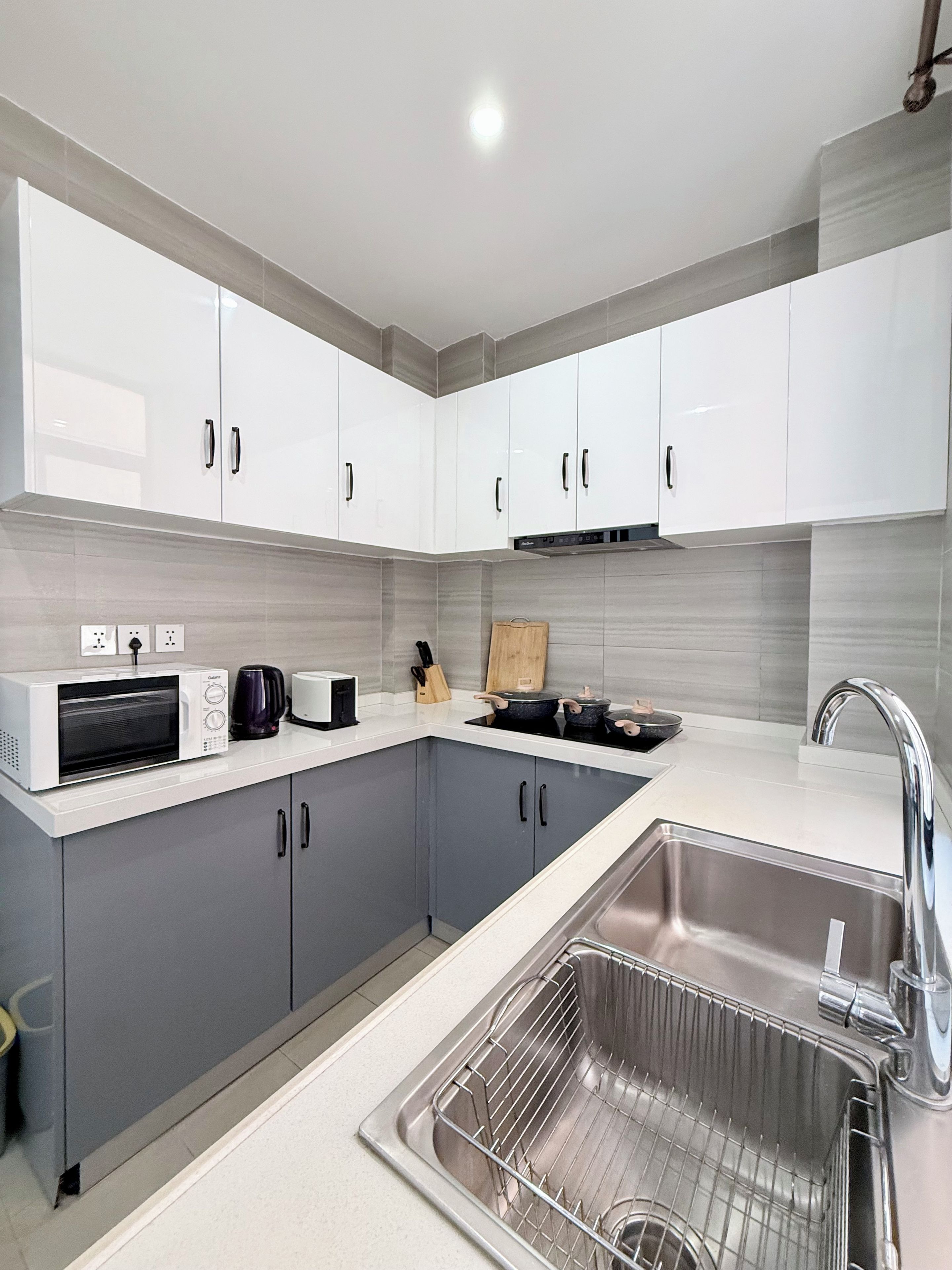 Una cocina moderna con gabinetes grises, un lavamanos de acero inoxidable y un microondas.