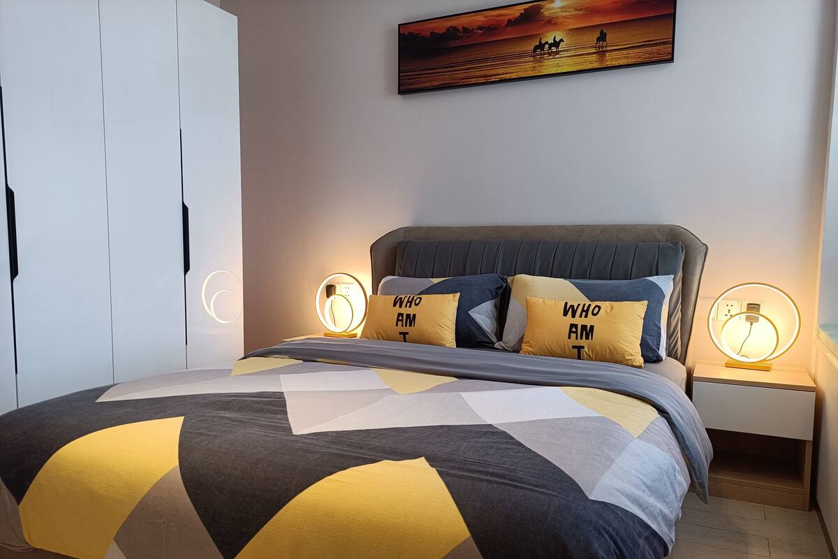 A modern bedroom with a large bed, two bedside tables with lamps, and a painting on the wall.