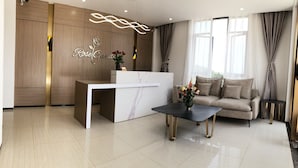 Uma área de recepção moderna com parede de painéis de madeira, balcão de mármore, um sofá e uma mesa de centro com flores.
