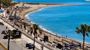 Un paysage urbain côtier avec une plage, des palmiers et un ciel bleu dégagé.