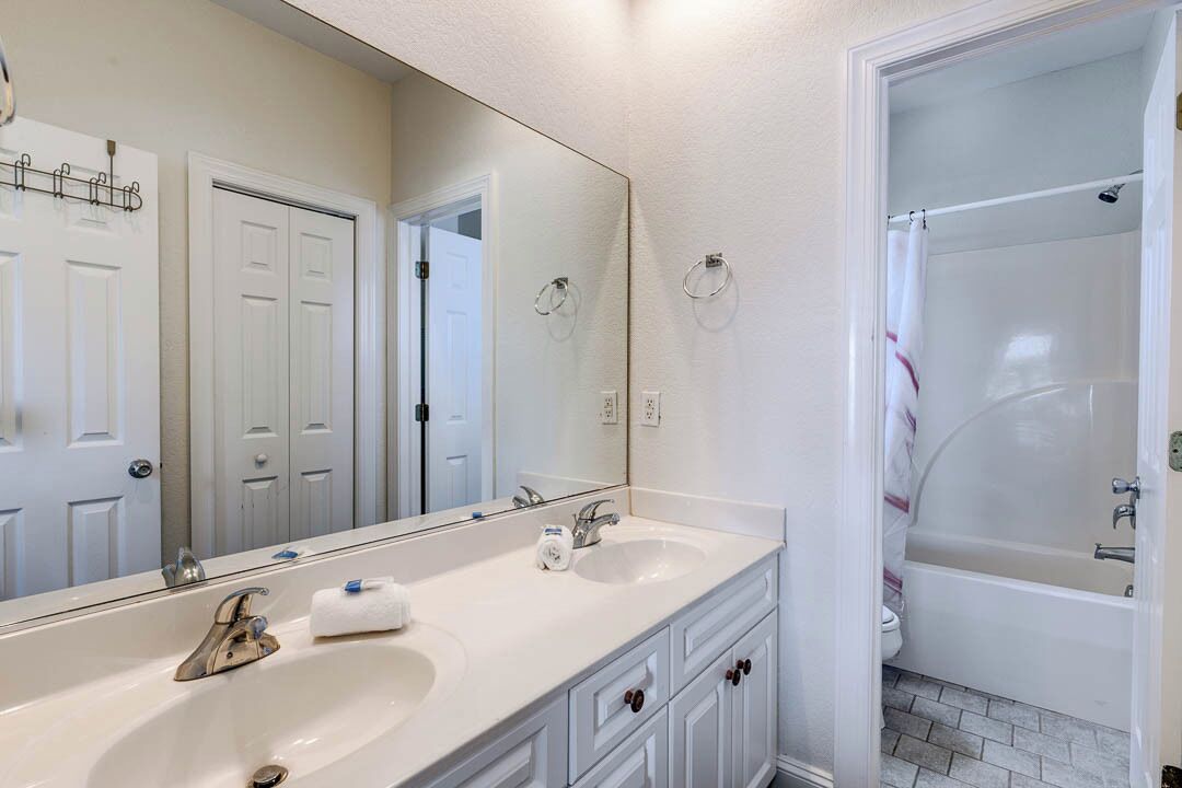 A bathroom with a double sink, a large mirror, a shower, and a toilet.