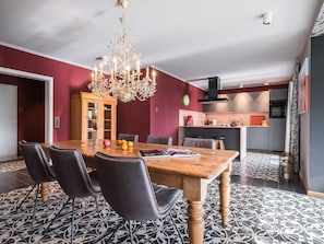 Ein Essbereich mit einem Holztisch und Stühlen, einer Chandelüster und einer Küche im Hintergrund.