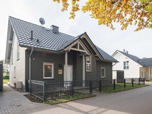 Ein modernes, zweistöckiges Haus mit grauer Fassade, einer Satellitenschüssel und einem eingezäunten Garten.