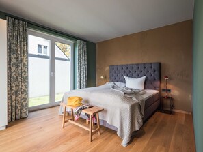 Ein Schlafzimmer mit einem Bett, einem Nachttisch, einer Lampe und Blick ins Freie.