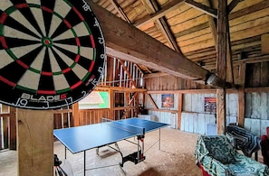A dartboard, a ping pong table, and wooden walls in a room.