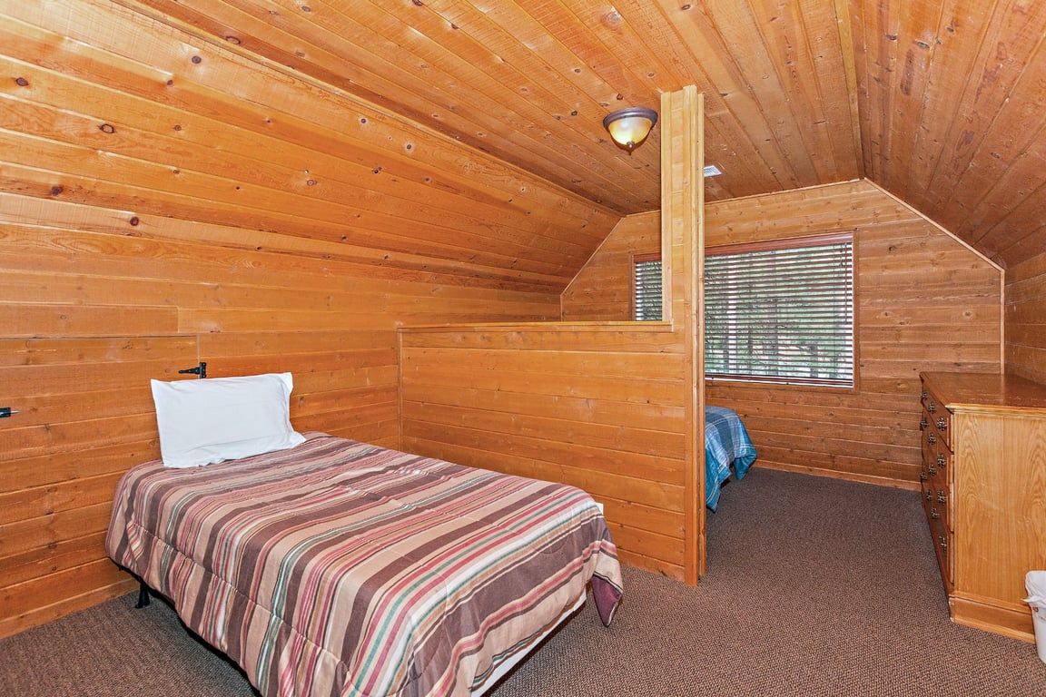 A bedroom with a bed, a dresser, a window with blinds, and a sloped ceiling.
