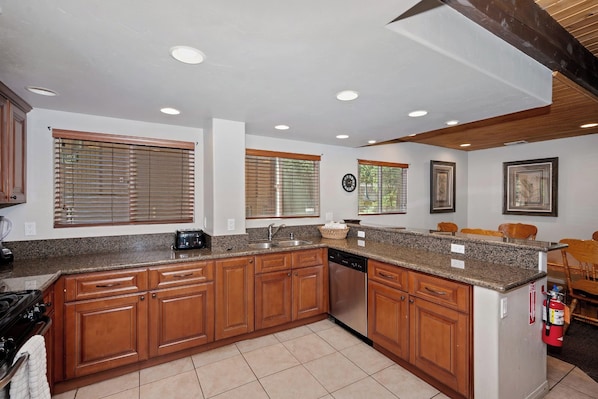 A kitchen with wooden cabinets, granite countertops, a stainless steel sink, and a built-in dishwasher.