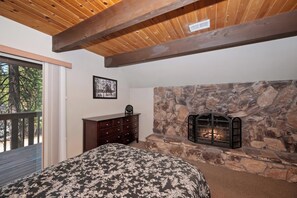 Un dormitorio con chimenea de piedra, techo de madera, cómoda y cama con colcha estampada.