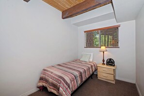 A bedroom with a bed, a nightstand, a lamp, and a window with blinds. - Redwood Lodge by Destination Big Bear : Close to Snow Summit and Short Drive to Lake & Village! Air Hockey! (Big Bear Lake)