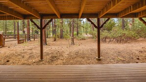 A covered wooden deck with a view of a forested area.