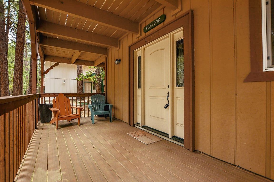 A wooden deck with a covered area, a door labeled 'REDWOOD', and two chairs.