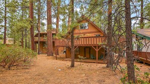 A cabin with a wooden deck, surrounded by tall pine trees.