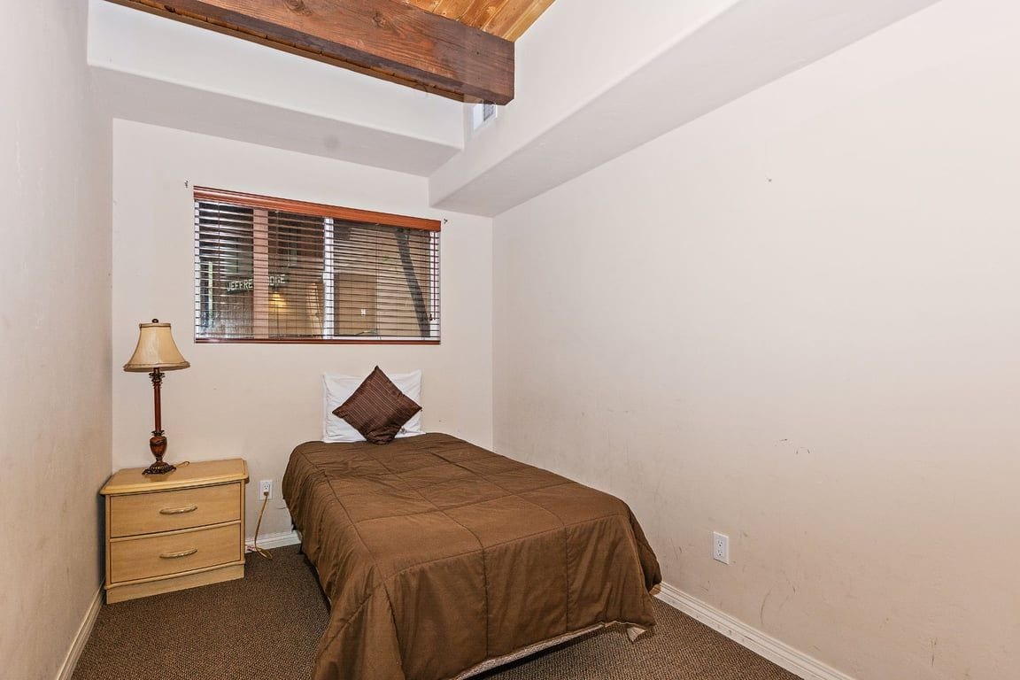 A bedroom with a bed, a nightstand, a lamp, and a window with blinds.