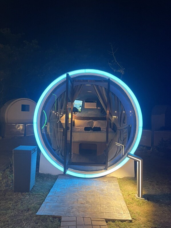 A circular structure with a bed inside, illuminated by blue lights, and a pathway leading to it. - Cocoons Casobe (Calatagan)
