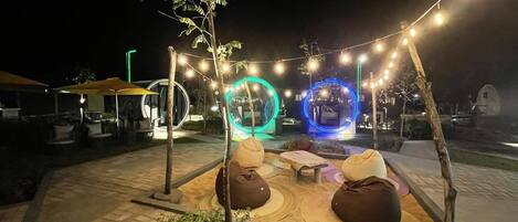 An outdoor seating area with circular light installations, string lights, and a small tree.