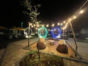 An outdoor seating area with circular light installations, string lights, and a small tree. - Cocoons Casobe (Calatagan)