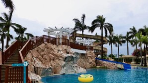 A pool area with a rock formation, stairs, and palm trees. - Cocoons Casobe (Calatagan)