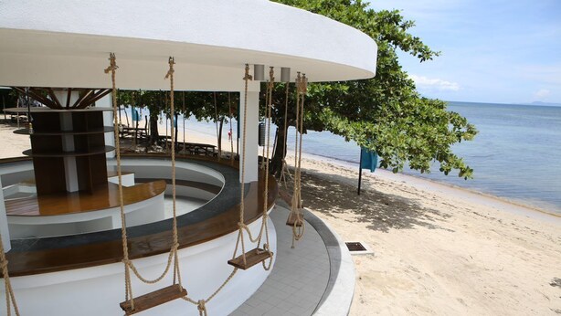 A circular outdoor seating area with swings and a central pillar, overlooking a beach. - Cocoons Casobe (Calatagan)